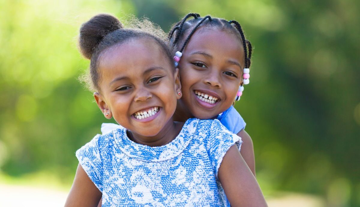 Two young sisters hugging and smiling for the camera.